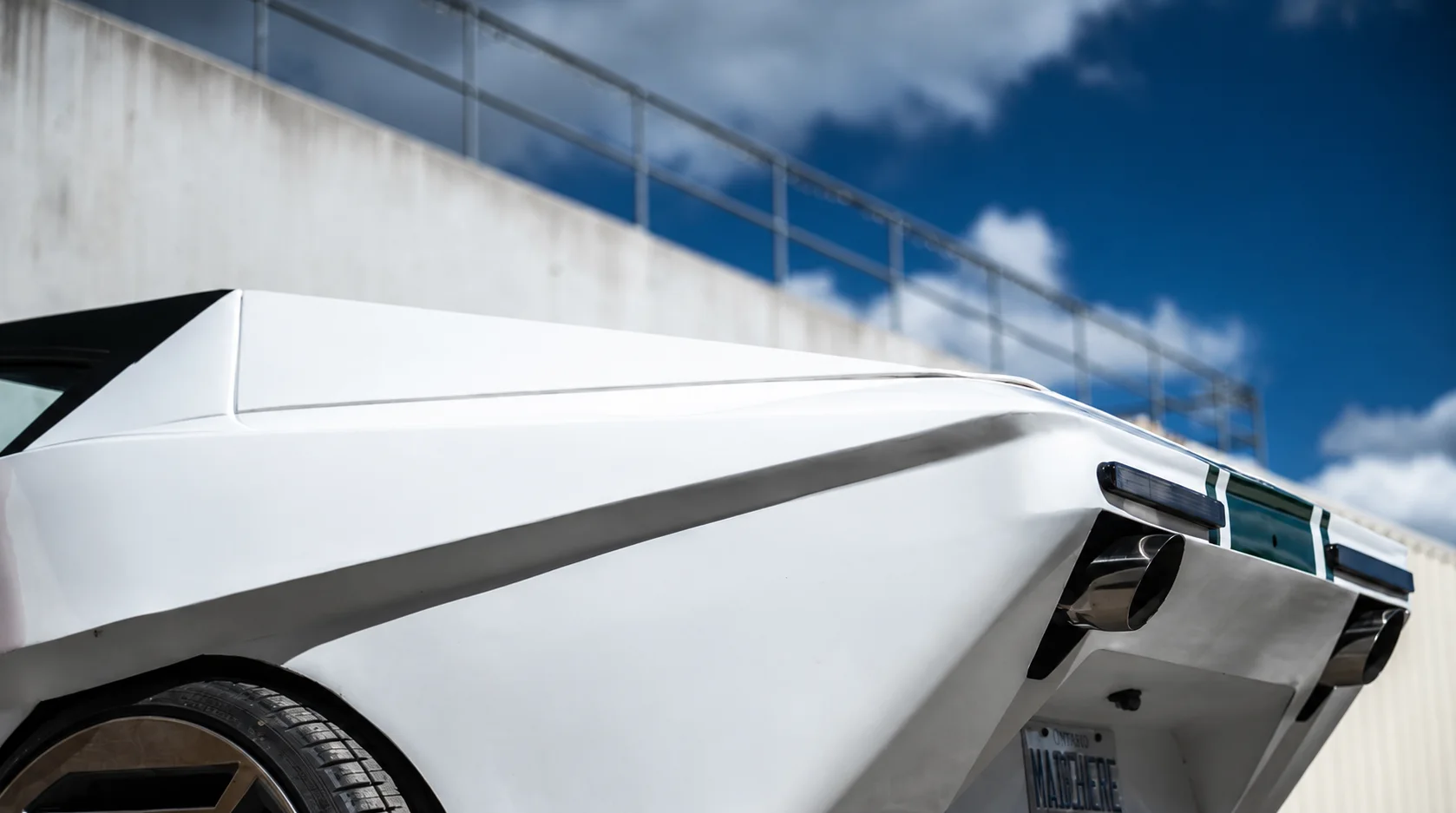 Rear three-quarter view of the LITT concept car, its sculpted white bodywork catching daylight against a concrete overpass.