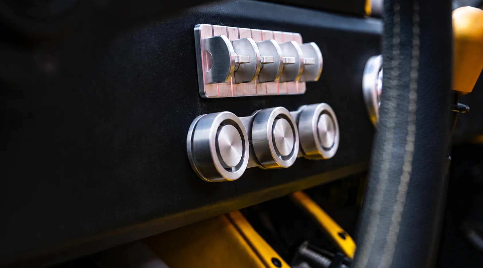 Close-up of the LITT cabin: a row of machined metal toggle switches above three knurled aluminium dials.